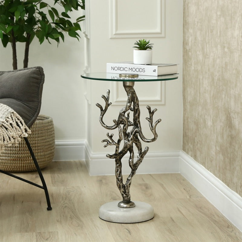 Decorative side table with metal base and glass top in a room setting.