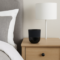 Black vase on a wooden nightstand next to a bed with gray and white bedding.