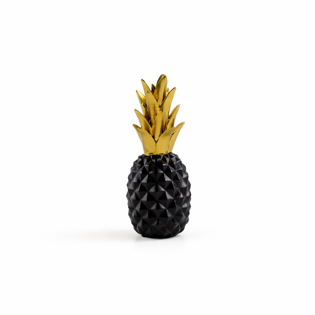 Close-up of a matte black pineapple ornament with a shiny gold crown on a dark wood sideboard.
