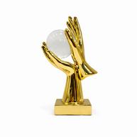 Gold-finish hands holding a clear crystal sphere on a white background.