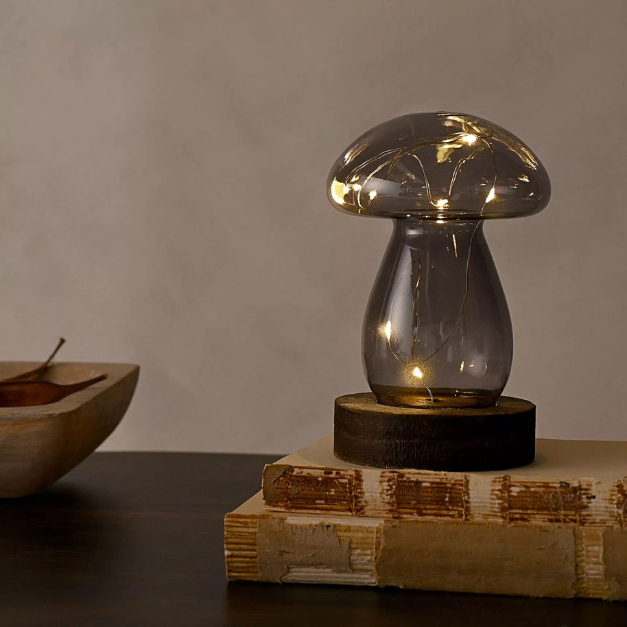 Grey Glass Mushroom on a oak wood side table on top of 2 books with a taupe wall background