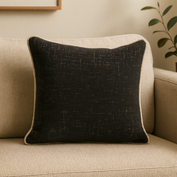 Black textured pillow on a beige couch with a plant in the background