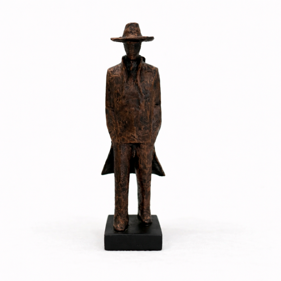 Textured bronze sculpture of a lone figure in a long coat and hat, styled on a modern concrete-topped console table.