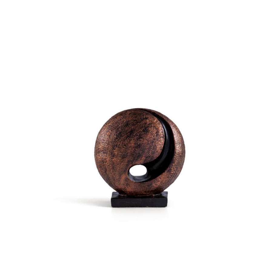 Bronze abstract moon sculpture with a hollow center and black base, styled on a minimalist bookshelf.