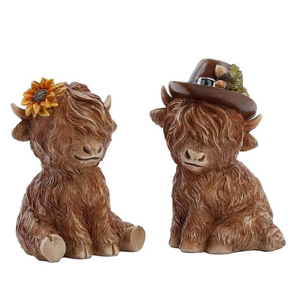 Two small Highland Cow figurines, one with a hat and one with a sunflower, displayed together on a white background.