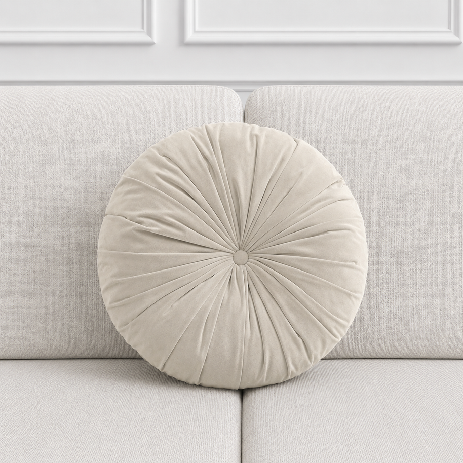 Round pleated beige pillow on a light gray sofa with a white paneled wall background