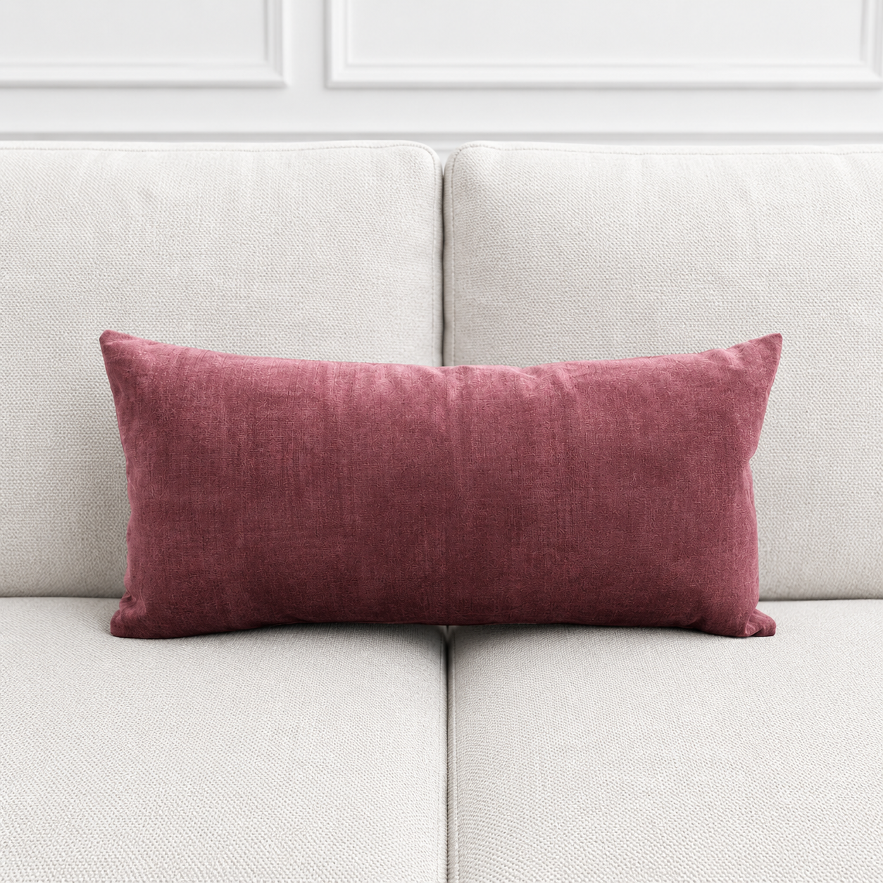 Maroon pillow on a light gray sofa against a white paneled wall